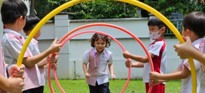 A young child practicing balance and coordination by walking carefully along a fallen tree log in the forest.
